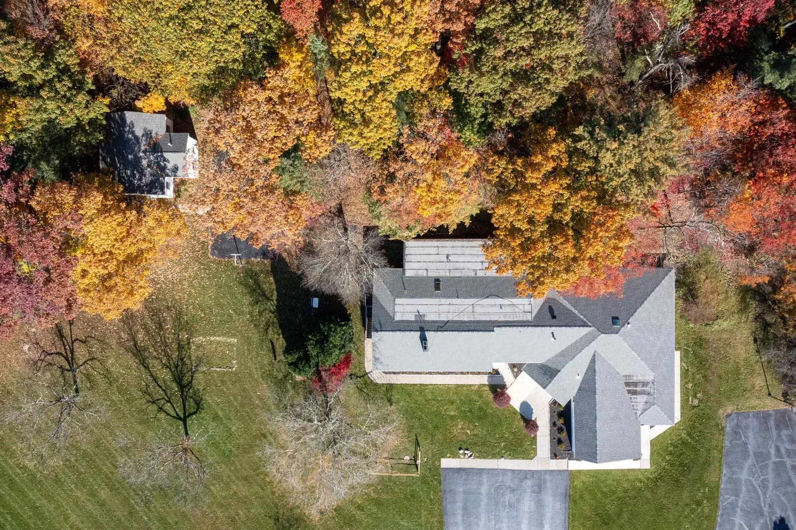 The image shows a residence with a prominent front porch during autumn, surrounded by trees with vibrant fall colors.