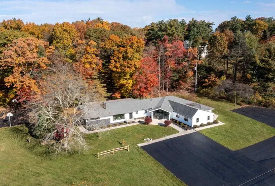 The image shows a two-story house with a shingled roof, set amidst autumn foliage on a clear day.